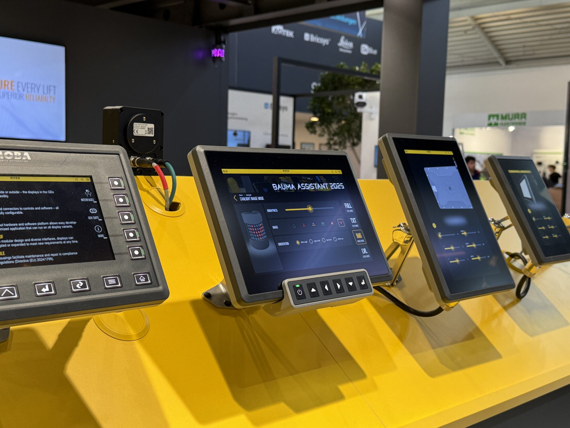 Row of yellow-framed touchscreen kiosks at a trade show, displaying software interfaces on their screens with a bright yellow booth backdrop.
