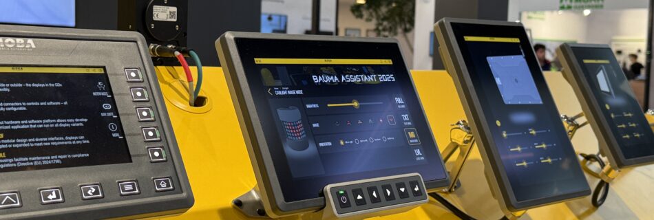 Row of yellow-framed touchscreen kiosks at a trade show, displaying software interfaces on their screens with a bright yellow booth backdrop.