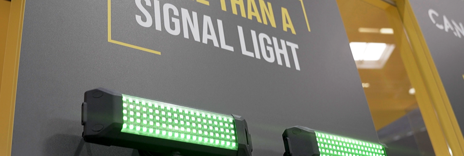 Sign reading 'MORE THAN A SIGNAL LIGHT' on a gray panel, with two green LED light bars below (industrial exhibit).