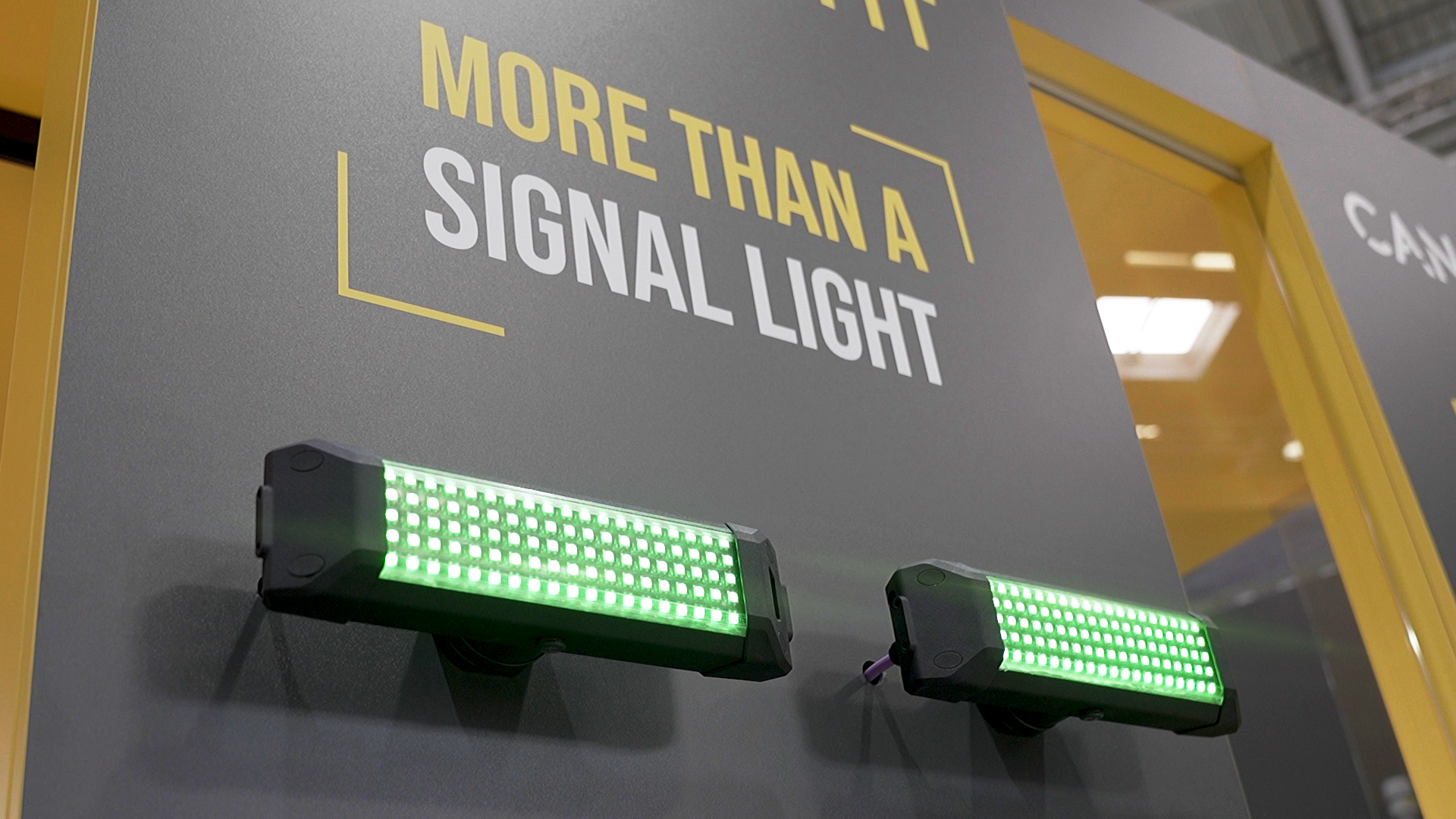 Sign reading 'MORE THAN A SIGNAL LIGHT' on a gray panel, with two green LED light bars below (industrial exhibit).