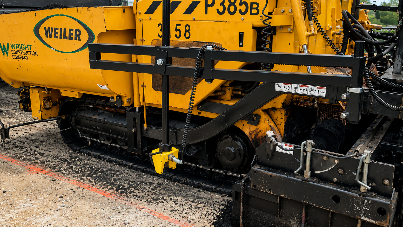 Close-up of a yellow asphalt paver with the WEILER logo and guard rails, on a construction site.